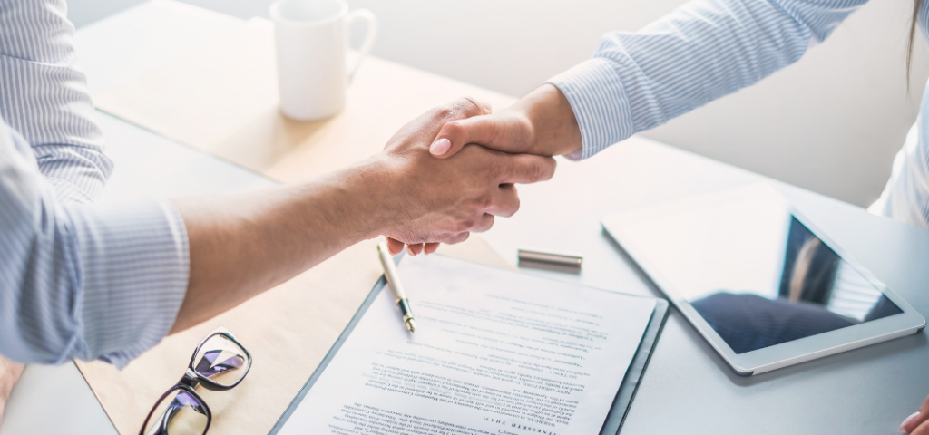Poignée de main entre deux personnes au-dessus d’un contrat de travail posé sur un bureau.
